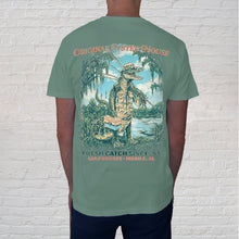 Load image into Gallery viewer, Fishing Gator Light Green Tee:  features a towering fishing gator standing near the swampy waters of the Mobile Delta, framed by moss-draped oaks. It’s part folklore, part Southern and all in for gator lovers. 
